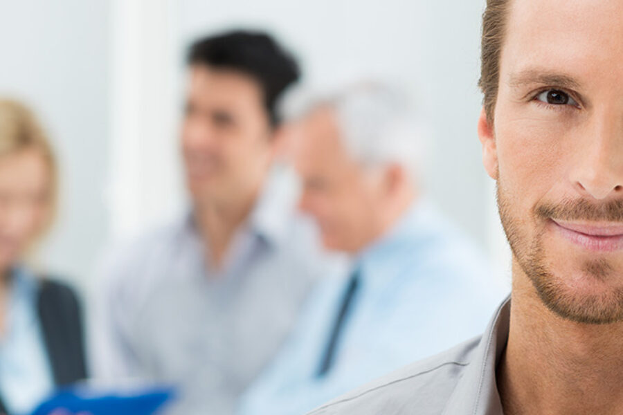 Portrait Of Young Handsome Businessman In Office With Colleagues in The Background